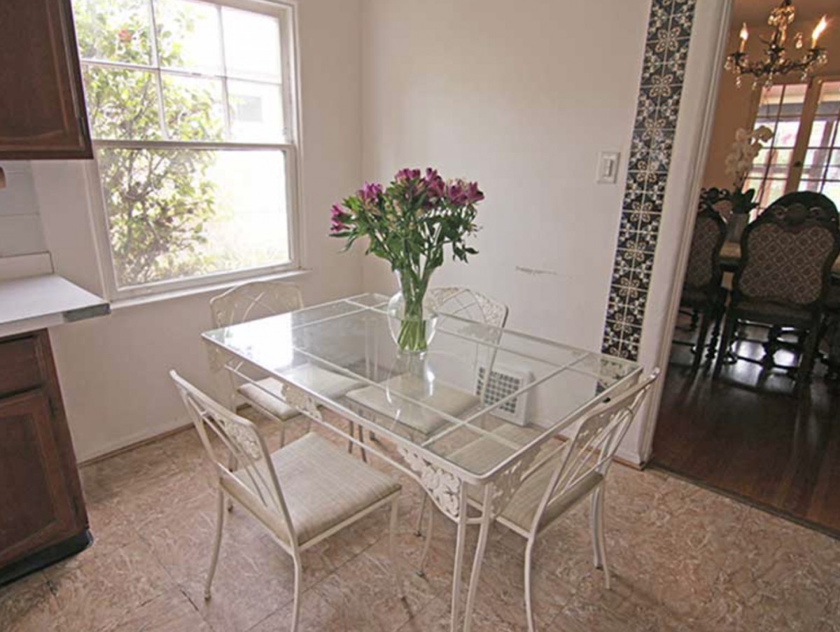 A cozy dining area with a glass table and chairs, adorned with a vase of flowers by a sunlit window.