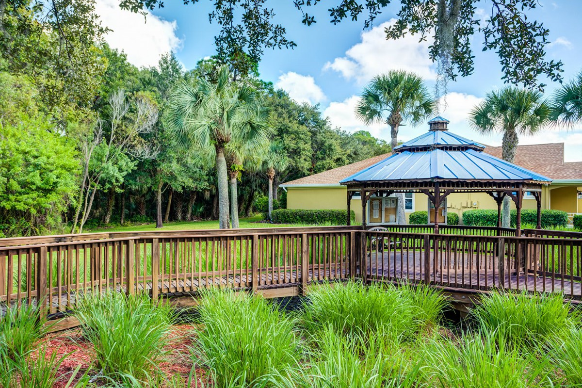 A serene garden featuring a wooden gazebo and bridge surrounded by lush greenery and trees.
