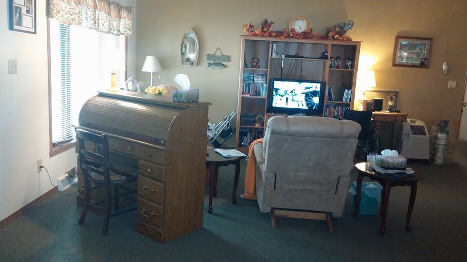 A cozy living room with a desk and bookshelf, featuring a television and a comfortable chair.
