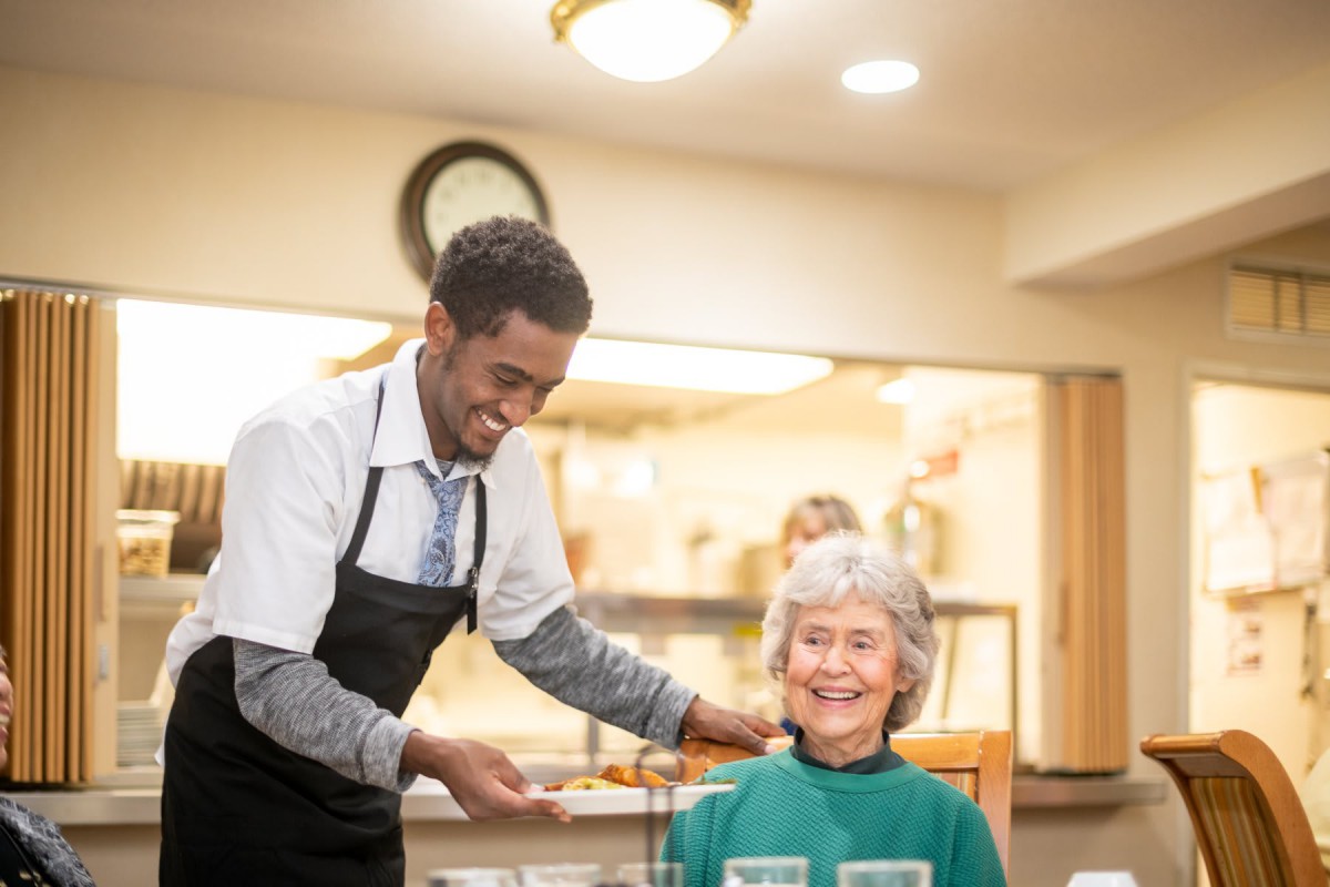 A waiter serves a smiling elderly woman at a restaurant.