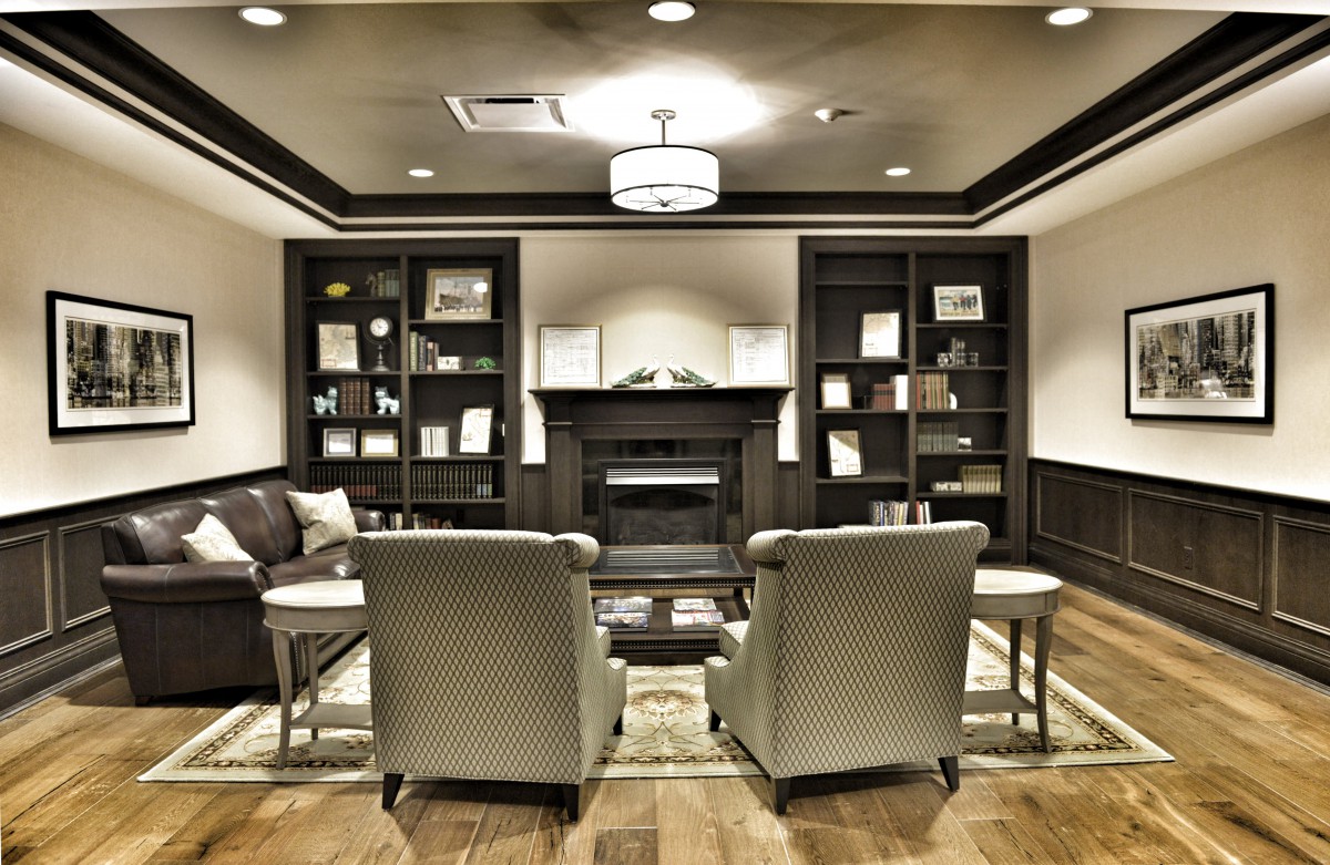A modern living room interior featuring a cozy seating area with armchairs, a central fireplace, and bookshelves on either side.