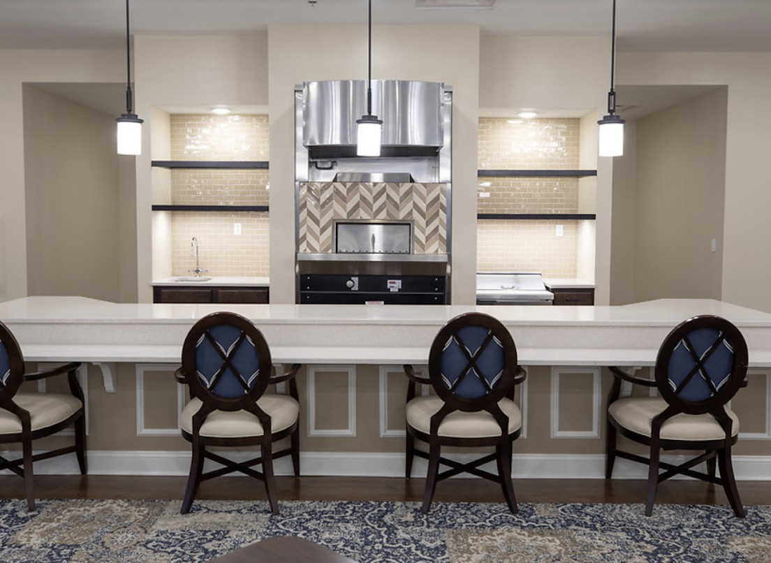 A modern kitchen with a sleek design featuring a large countertop, bar stools, and pendant lighting.
