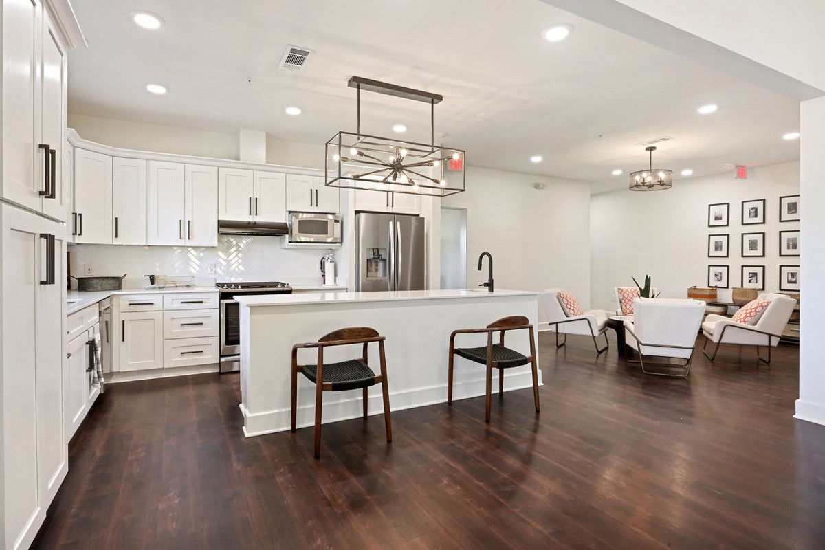 A modern kitchen with white cabinets, stainless steel appliances, and an open concept design featuring hardwood floors and an island counter with wooden chairs.