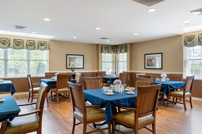A neatly arranged dining room with blue tablecloths and wooden chairs.