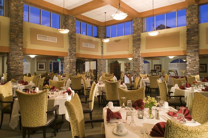 An elegant restaurant dining area with neatly arranged tables and chairs, illuminated by warm lighting.