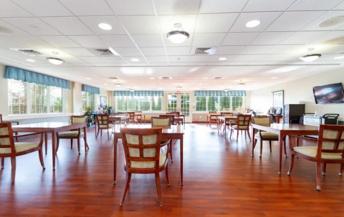 A spacious and bright dining room with wooden floors, neatly arranged tables, and chairs.