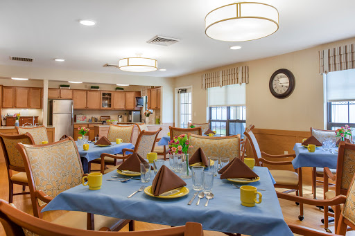 A well-set dining room with a cozy atmosphere, featuring a blue tablecloth, neatly arranged napkins, and a view of the kitchen.