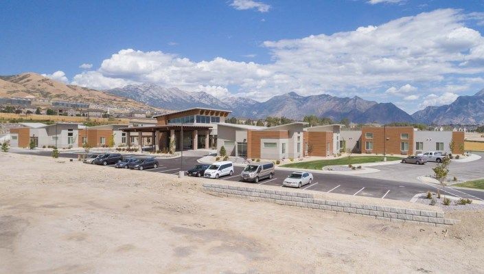 A modern building with a parking lot set against a backdrop of mountains and a blue sky.