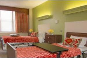 A hospital room with two neatly made twin beds and bright green walls.