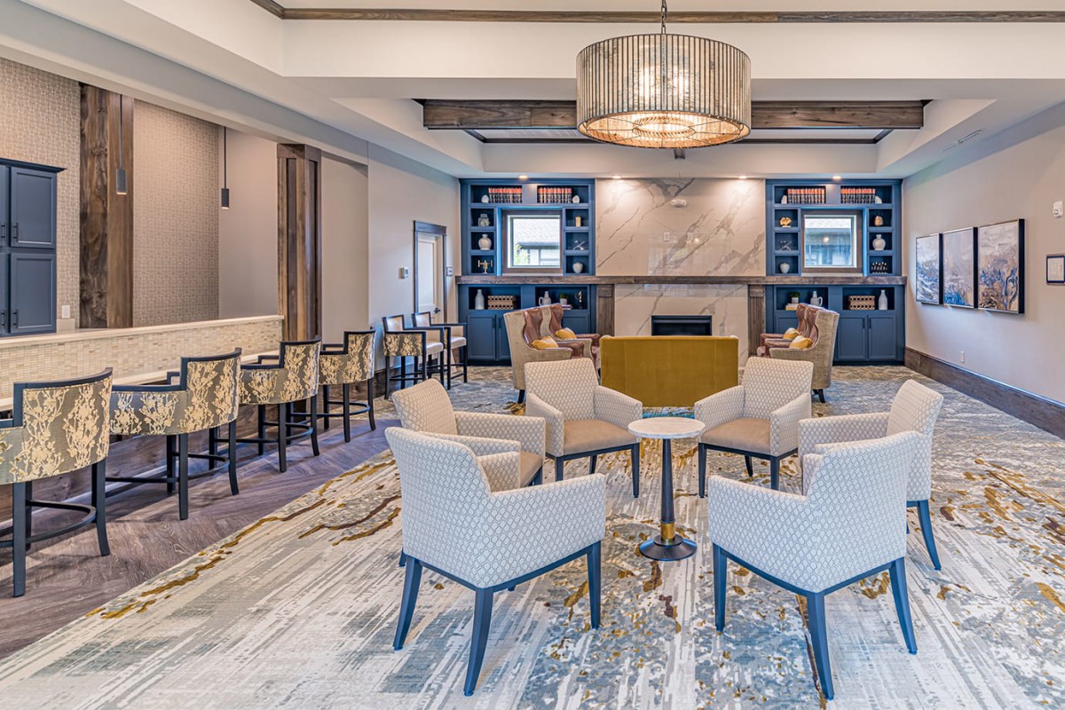 A modern lounge area featuring comfortable seating around a fireplace, accompanied by bookshelves and a stylish chandelier.