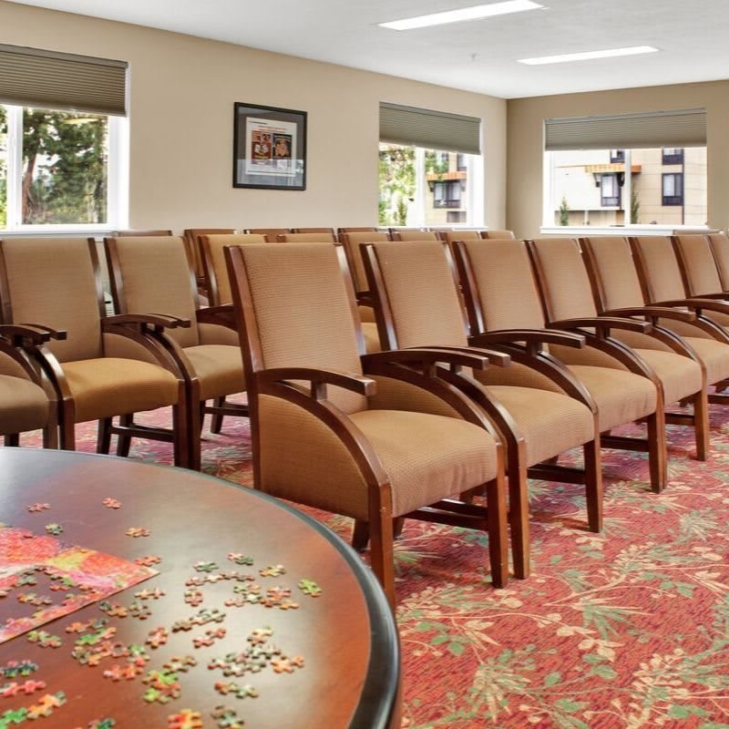 A well-arranged conference room with several rows of chairs facing a focal point, complemented by patterned carpet and natural light streaming through the windows.
