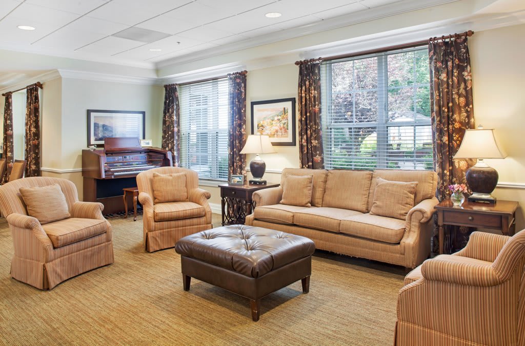 A cozy living room with comfortable seating and a piano by the windows.