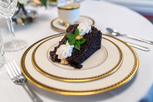 A decadent slice of chocolate cake topped with whipped cream and mint leaves, elegantly presented on fine china.
