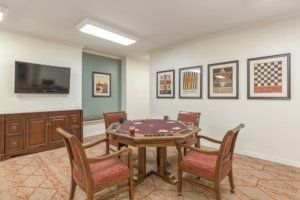 A cozy game room featuring a poker table surrounded by chairs, with artwork and a television on the walls.