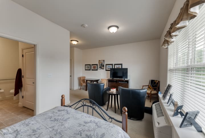 A cozy living and sleeping area featuring a bed, seating arrangement with leather chairs, a TV, and wall decor.