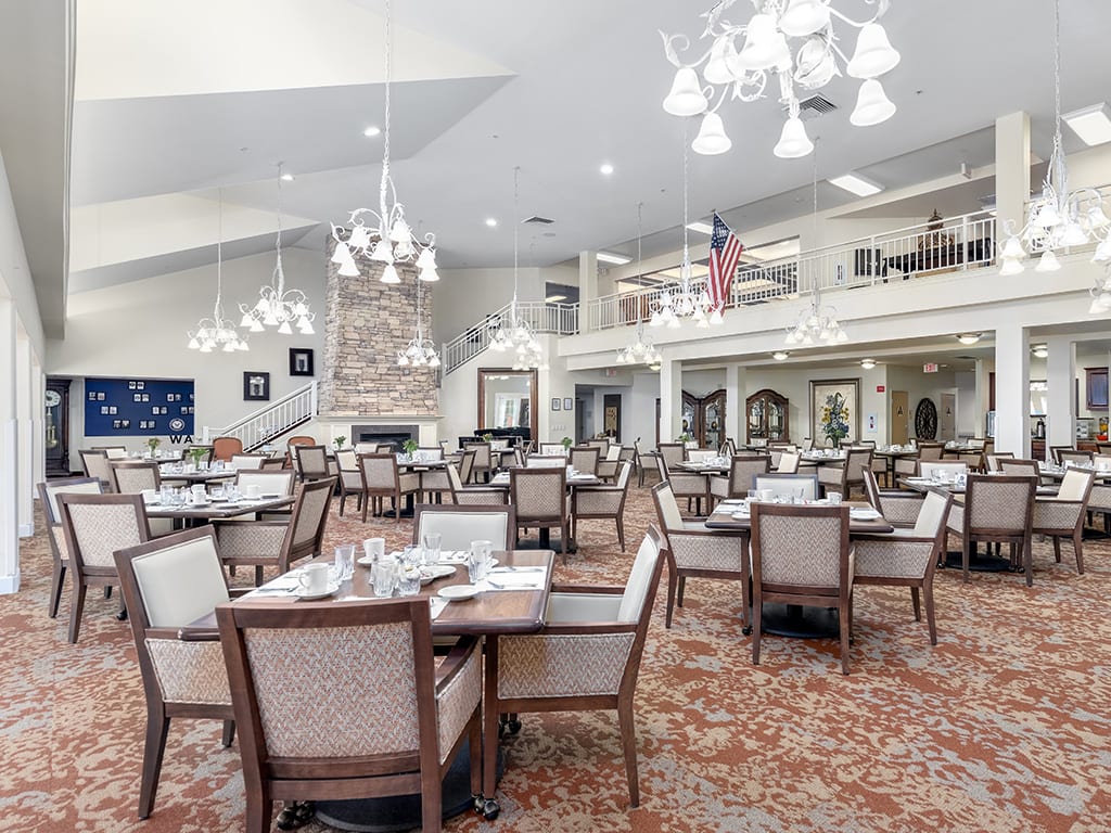 A spacious and elegantly designed dining room with neatly arranged tables and chairs, featuring bright chandeliers.