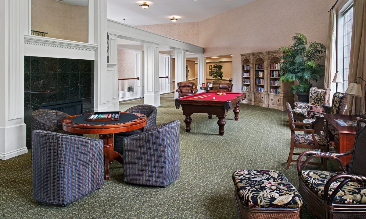 A spacious game room featuring a billiards table, bookshelves, and comfortable seating.