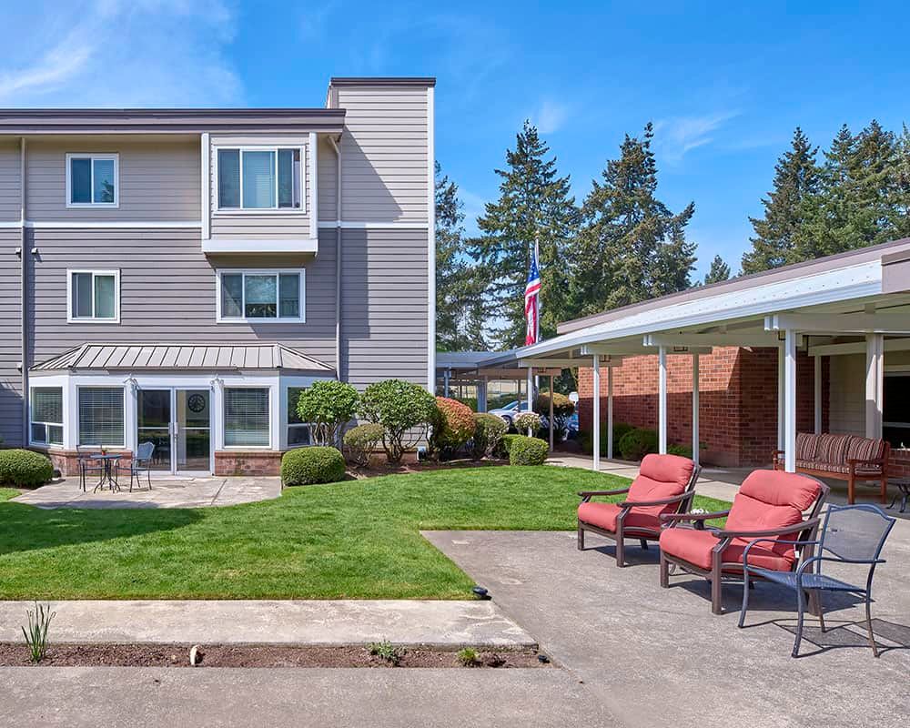 A sunny exterior view of a building with a well-maintained lawn and comfortable outdoor seating.