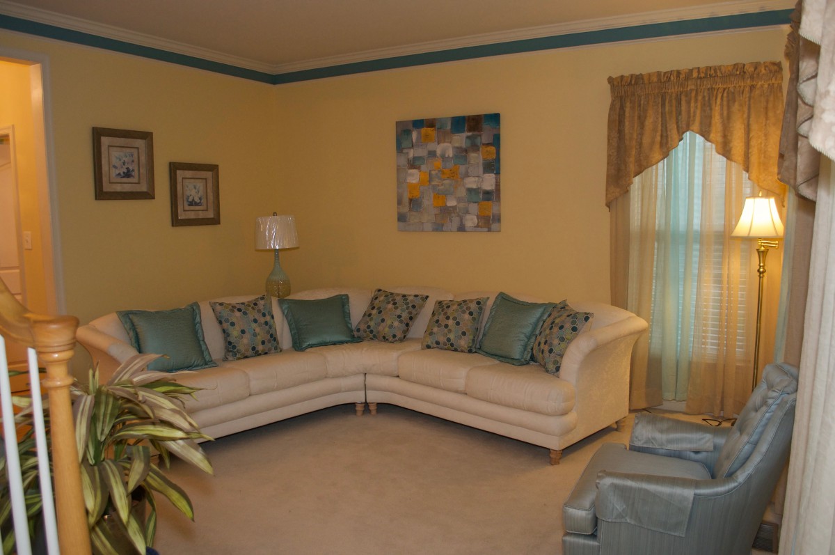 A cozy living room featuring an L-shaped sofa with decorative cushions, complemented by artwork and a lamp against yellow walls.