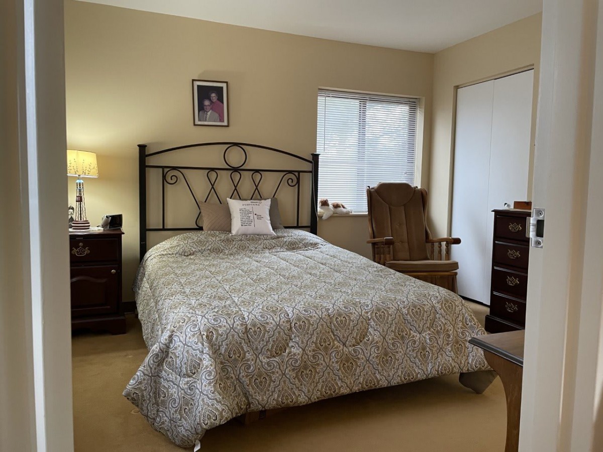 A cozy bedroom with a neatly made bed, a lamp on a nightstand, a rocking chair, and a dresser.