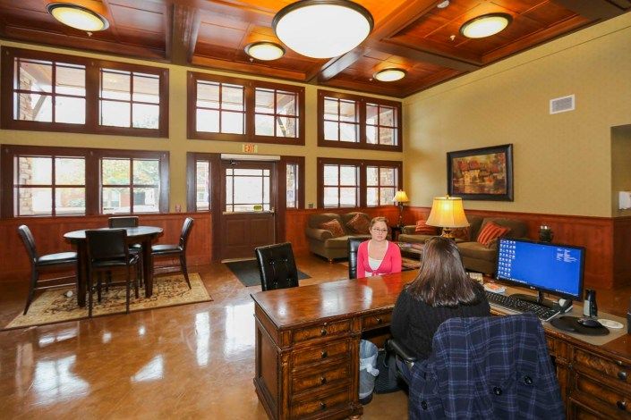 A welcoming office reception area with a wooden ceiling, featuring a desk where two people are seated and a cozy lounge space in the background.