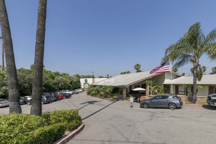 A hotel entrance with a parking lot and palm trees on a sunny day.