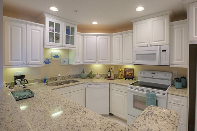 A modern kitchen with white cabinets and granite countertops, featuring built-in appliances and well-lit spaces.