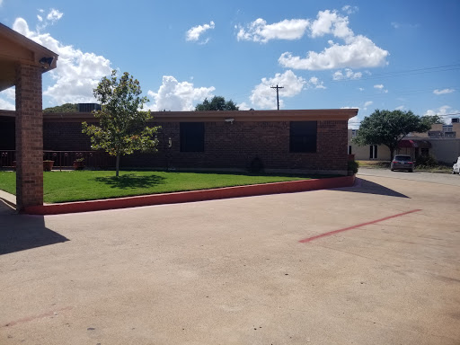 A sunny day view of a brick building with a landscaped parking area.