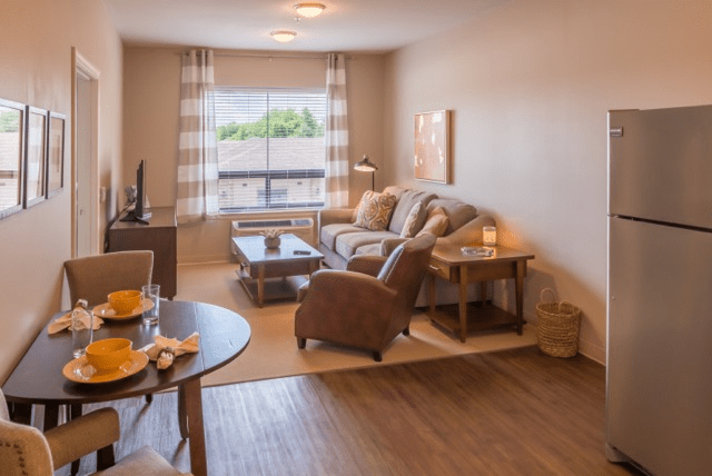A cozy living room with a comfortable sofa set and a coffee table, featuring soft lighting and large windows.