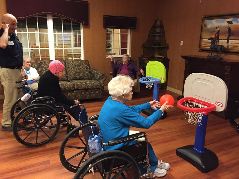 Elderly individuals in wheelchairs playing basketball indoors.