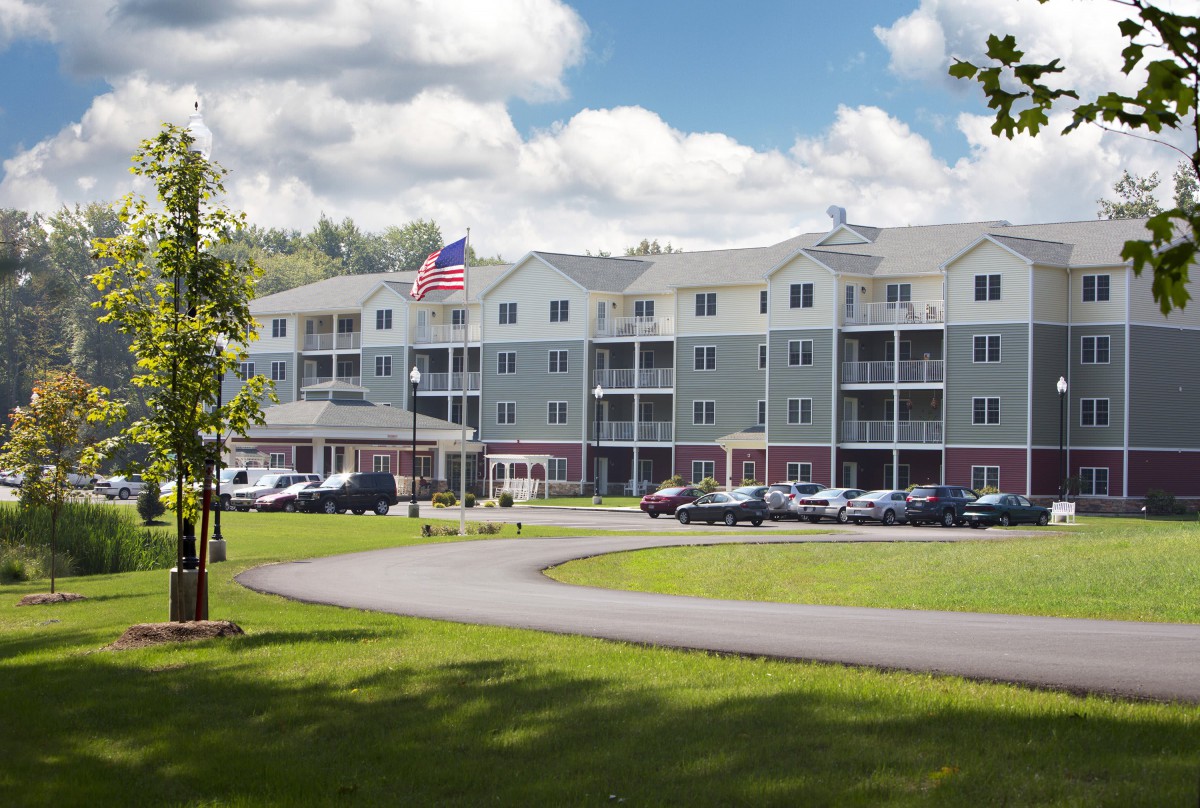 A multi-story residential building with a well-maintained lawn and parking lot under a cloudy sky.