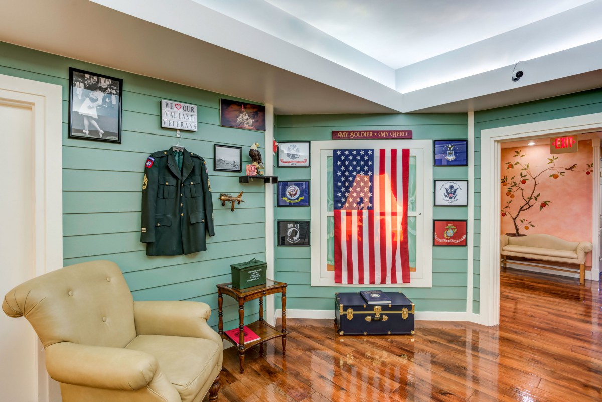 A room decorated with military memorabilia, featuring an American flag, a military uniform, framed photographs, and a vintage suitcase.