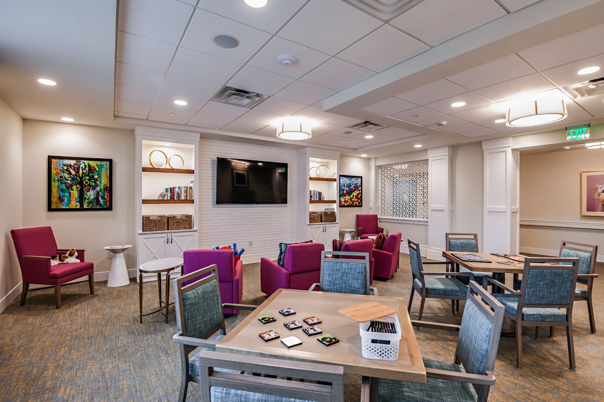A modern lounge area with comfortable seating, a television, and bookshelves, accented by vibrant decor.