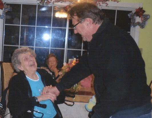 An elderly woman shares a joyful moment with a man indoors.
