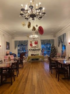 A festive dining room adorned with Christmas decorations, featuring elegant chandeliers and neatly arranged tables and chairs.