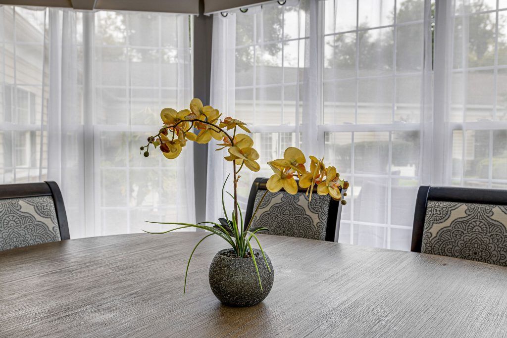 A vibrant yellow orchid in a vase on a wooden table, illuminated by natural light through large windows.