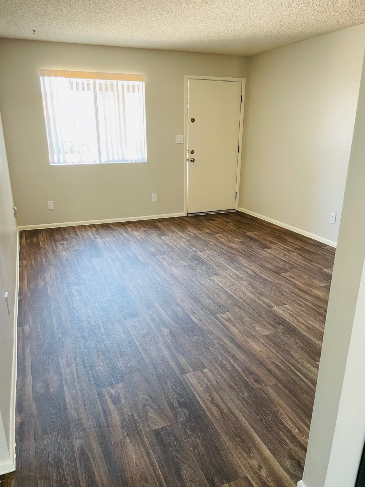 An empty room with hardwood flooring, featuring a window and a door.