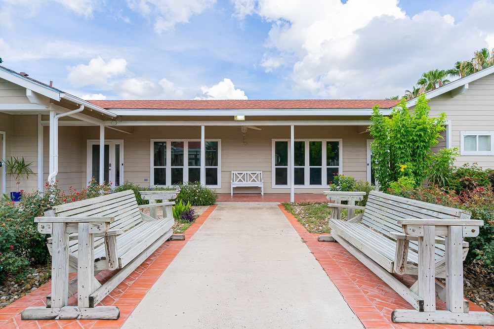 A serene courtyard with benches and a pathway leading to a building under a partly cloudy sky.