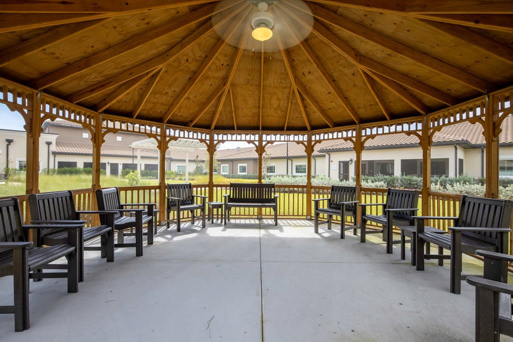 A wooden gazebo with benches arranged in a circle, situated in a landscaped area.