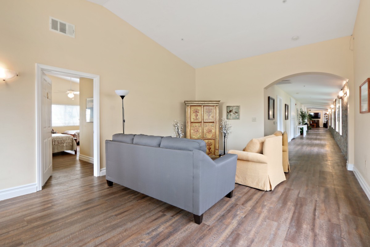 A cozy living room with a gray sofa, beige armchair, wooden cabinet, and standing lamp on hardwood flooring.