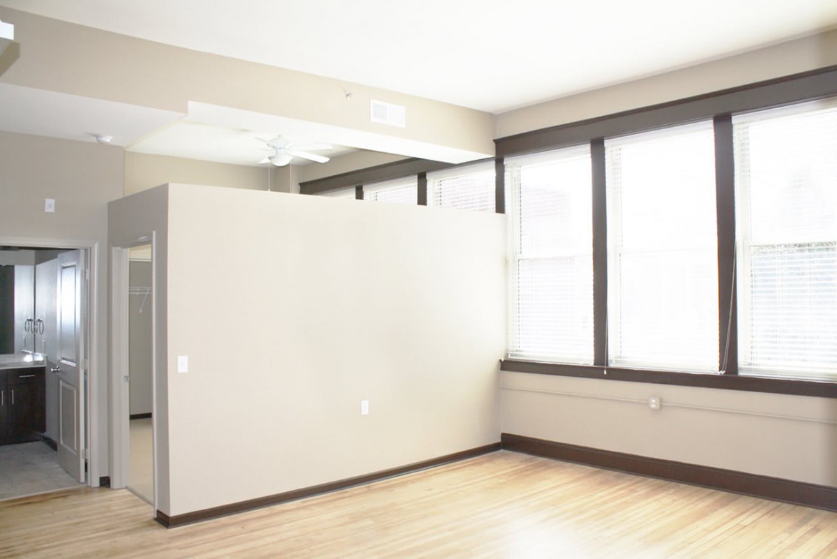 An empty apartment with large windows and hardwood flooring.
