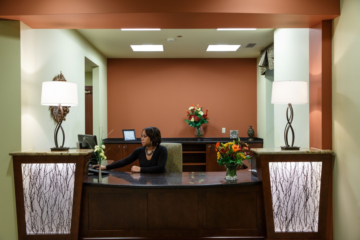A receptionist sits at the front desk in a well-decorated office lobby.