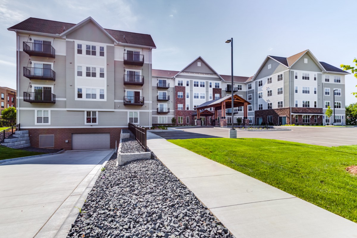A modern residential apartment complex with well-maintained landscaping and a paved pathway.