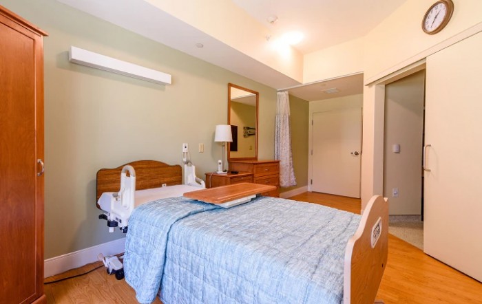 A well-equipped hospital room featuring a patient bed with a table, lamp, and mirror.