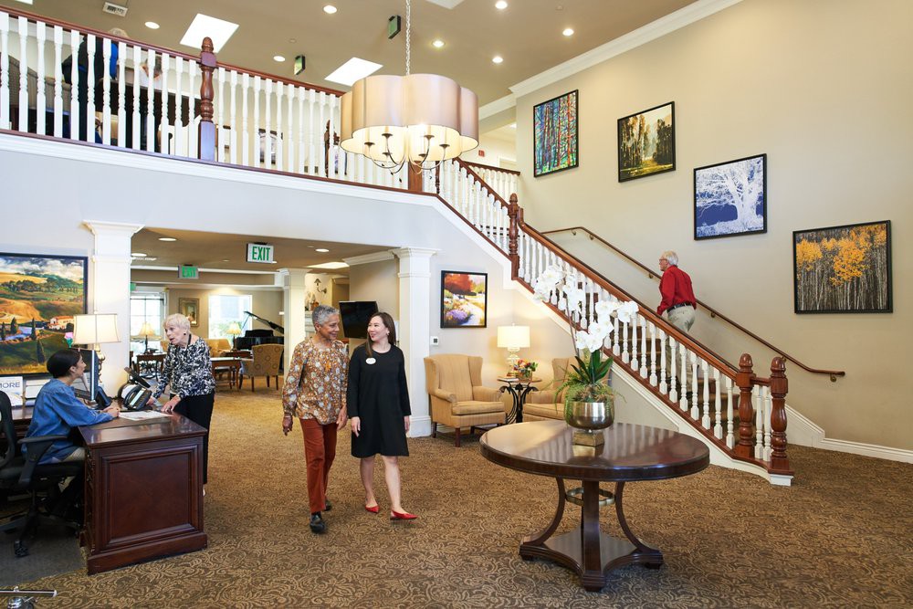 A spacious lobby with a grand staircase, multiple people walking and seated, and elegant decor.
