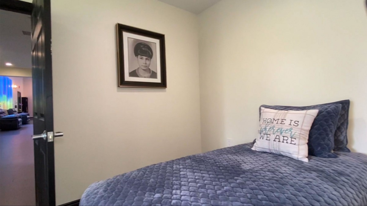 A minimalist bedroom with a bed covered in a blue quilt and a framed portrait on the wall.