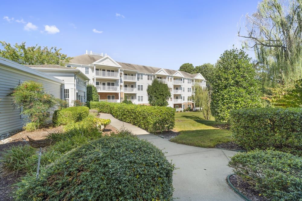 A residential apartment building surrounded by greenery and trees with a pathway in the foreground.