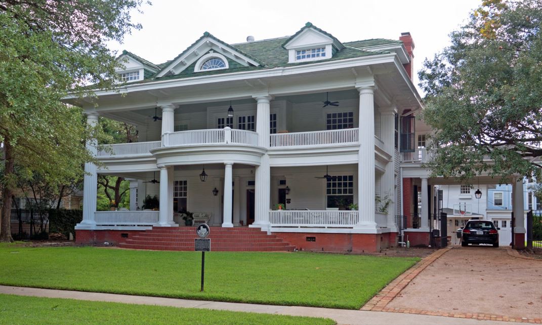 A historic colonial-style house with a large porch and manicured lawn.