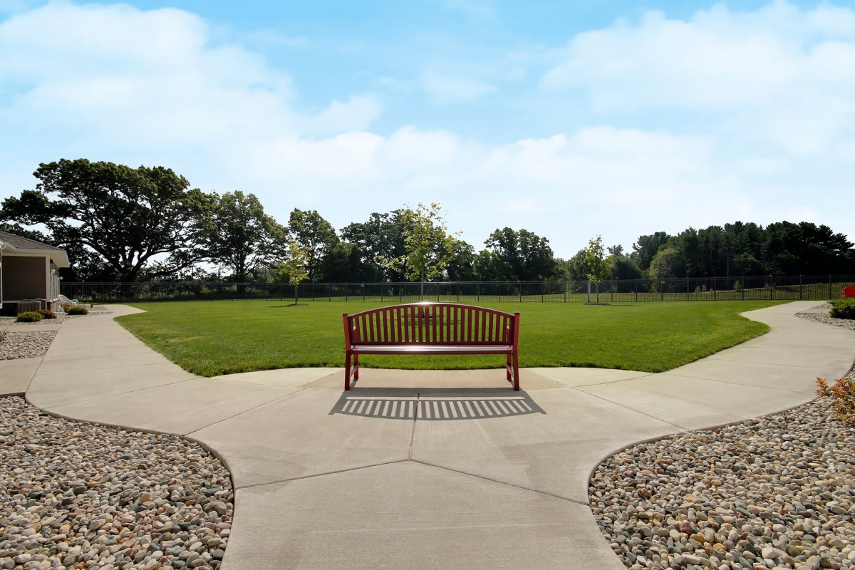 A wooden bench situated at the intersection of two pathways in a park with green grass and trees.