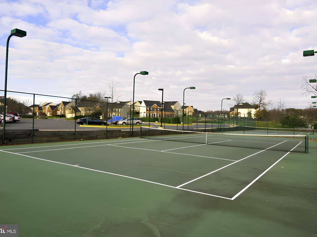 An outdoor tennis court located in a residential area under a cloudy sky.